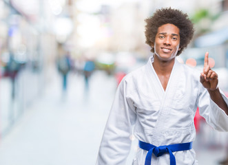 Afro american man wearing karate kimono over isolated background showing and pointing up with finger number one while smiling confident and happy. © Krakenimages.com