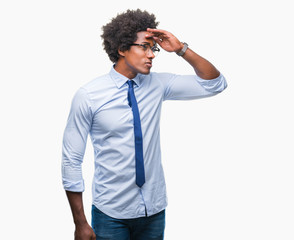 Afro american business man wearing glasses over isolated background very happy and smiling looking far away with hand over head. Searching concept.