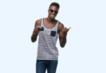 Young african american man holding vintage camera pointing with hand and finger up with happy face smiling