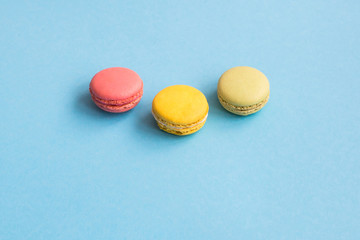 Top view of yellow, green and pink macarons or macaroons on turquoise background. Macaron from above, pastel colors.