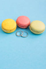 Wedding rings on macarons or macaroons on turquoise background top view. Macaron from above, colorful almond cookies, pastel colors