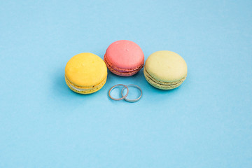 Wedding rings on yellow, green and pink macarons or macaroons on turquoise background top view. Macaron from above, pastel colors. Wedding concept
