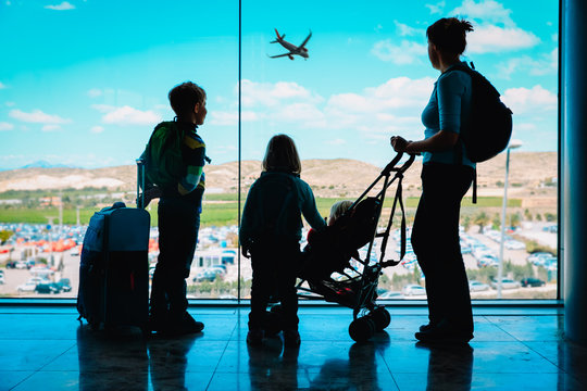 mother with kids and luggage looking at planes in airport