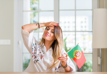 Young woman at home holding flag of Portugal stressed with hand on head, shocked with shame and surprise face, angry and frustrated. Fear and upset for mistake.