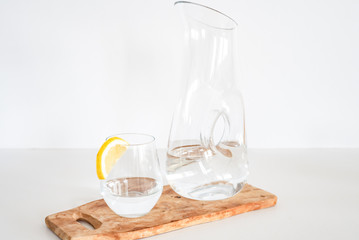 side view of glass and bottle of water with slice of lemon on a wood plate, white background