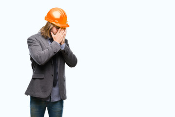 Young handsome architec man with long hair wearing safety helmet over isolated background with sad expression covering face with hands while crying. Depression concept.