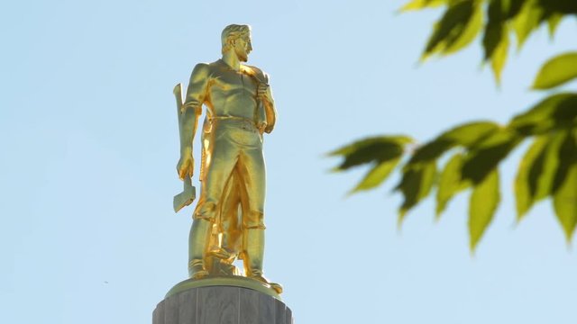 The gold Oregon Pioneer Man statue on top of the Oregon State Capitol building in Salem, tree branches in the right of the frame.