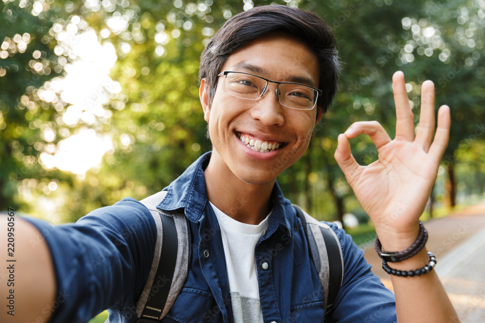 Sticker Smiling asian male student in eyeglasses making selfie