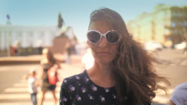 Young Beautiful Brunette Woman In Sunglasses Looking At Camera, Crowd Of People On Summer City Street In Background. Closeup, Shallow DOF, Slow Motion, 4K UHD.