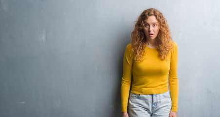 Fototapeta premium Young redhead woman over grey grunge wall scared in shock with a surprise face, afraid and excited with fear expression