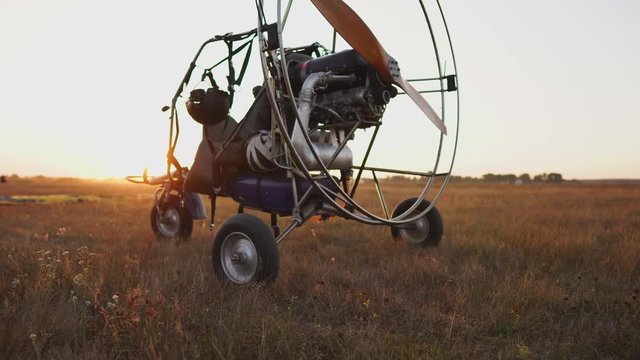 Motor paraglider stands at the airport in the rays of sunset sunlight. In the background, the plane takes off. The camera moves along the orbit