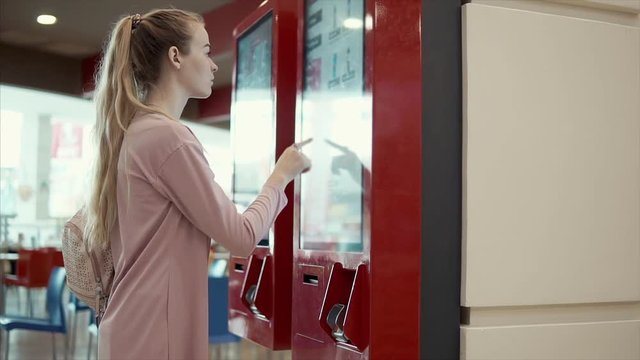 Female customer is using automat for ordering in fast-food cafe. Touching screen by hands, flipping up displays