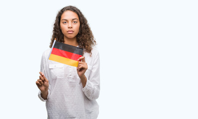 Young hispanic woman holding flag of Germany with a confident expression on smart face thinking serious