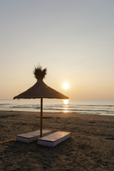 Beach chair and umbrella made from reed against wonderful sunrise over the sea with golden sun