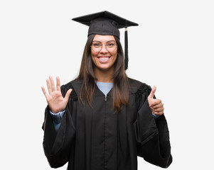 Young hispanic woman wearing graduated cap and uniform showing and pointing up with fingers number six while smiling confident and happy.