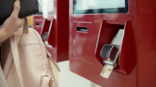 Girl buyer is inserting bank card in payment automat. She is putting pin code, taking off a bill, waiting an order