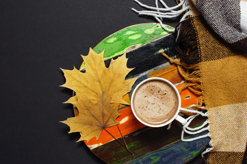 Obraz na płótnie Canvas Cup of hot chocolate, cocoa or coffee on vintage multi-colored wooden board with yellow autumn leaves, brown checkered plaid top view. Autumn flat lay background. Concept of warm cozy autumn