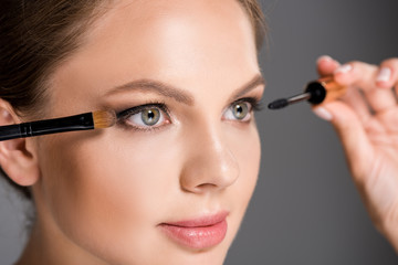 portrait of elegant woman with mascara and makeup brush for eyeshadows isolated on grey