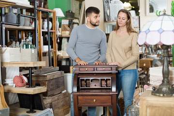 Thoughtful couple choosing vintage writing cabinet