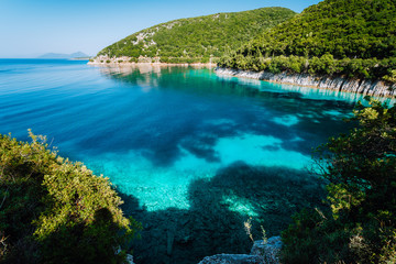 Azure bay. Picturesque scenery of the cove with turquoise calm water, surrounded by hills with cypresses, pine and olive trees. White limestone cliffs mirrow in the crystal clear water
