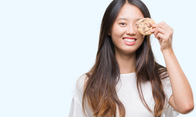 Young asian woman eating chocolate chip cookie over isolated background with a happy face standing and smiling with a confident smile showing teeth