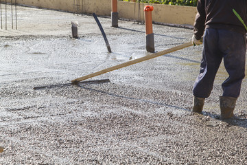 worker leveling fresh concrete slab with a special working tool