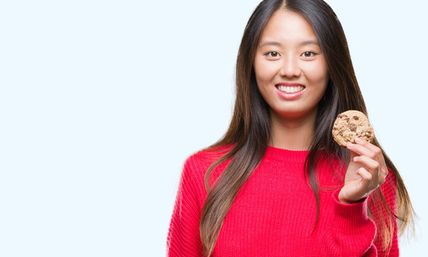 Young asian woman eating chocolate chip cookie over isolated background with a happy face standing and smiling with a confident smile showing teeth