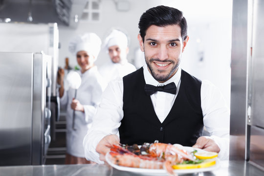 Waiter with dish of seafood in kitchen on restaurant