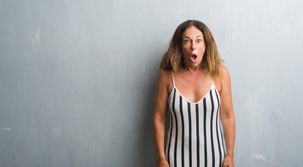 Fototapeta premium Middle age hispanic woman standing over grey grunge wall scared in shock with a surprise face, afraid and excited with fear expression
