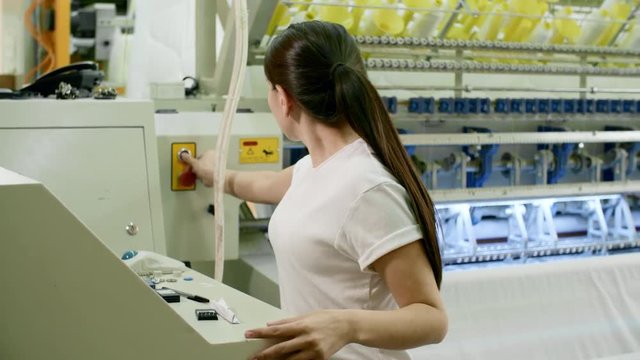 Beautiful brunette woman turning on industrial textile machine at plant and then looking at camera and smiling