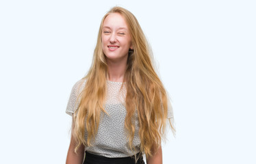 Blonde teenager woman wearing moles shirt winking looking at the camera with sexy expression, cheerful and happy face.
