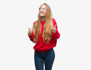 Blonde teenager woman wearing red sweater success sign doing positive gesture with hand, thumbs up smiling and happy. Looking at the camera with cheerful expression, winner gesture.