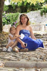 Happy mother and daughter sat down on a stone path to relax after a walk