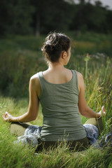 yogin girl sits in a meditative position at sunsat and moon rise on the picturesque shore of the lake. hands in mudra. Green juicy grass and a calm water surface surrounds it.