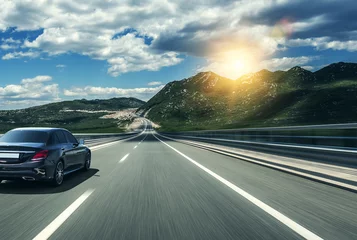 Foto op Plexiglas Snelle auto Zwarte auto haasten langs een hogesnelheidsweg in de zon.