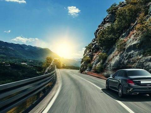 Black car rushing along a high-speed highway in the sun.