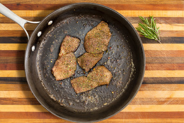 Pan containing roasted steak next to green herbs
