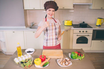 Nice and positive girl stands and poses. She holds wooden spoonin left hand. She shows big thumb up...