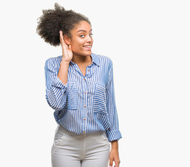 Young afro american woman over isolated background smiling with hand over ear listening an hearing to rumor or gossip. Deafness concept.