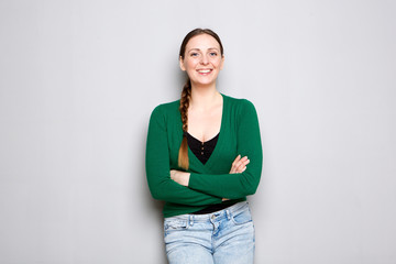 happy young woman standing by gray wall with arms crossed