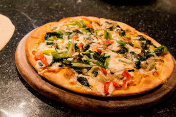 Delicious, cheesy and freshly baked colorful Italian vegetarian spinach, mushroom, bell pepper and vegetable pizza with mozzarella and Parmesan cheese on a wooden board. Selective focus.