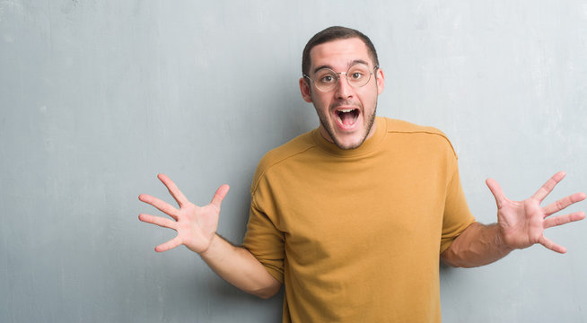 Young caucasian man over grey grunge wall very happy and excited, winner expression celebrating victory screaming with big smile and raised hands
