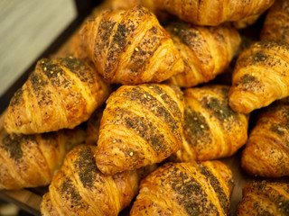Assortment of delicious and buttery croissants sprinkles with dried herbs, made by pastry chef on a wooden board, ready for sale. All look very tasty and delightful. Warm light.