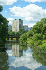 Fototapeta na wymiar Reflection of clouds in the water. River chertyanka and a natural park on the background of residential buildings in Moscow.