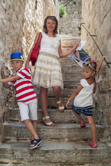 concept of travelling with children. beautiful woman holding a travel guide next to her children stand on the street of the old town of Kotor, Montenegro