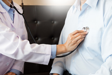 Doctor listening to cheerful young patients chest with stethoscope in his office at the hospital