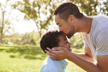 Close Up Of Father Kissing Son In Park - obrazy, fototapety, plakaty