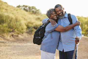 Portrait Of Senior Couple Wearing Backpacks Hiking In Countryside Together