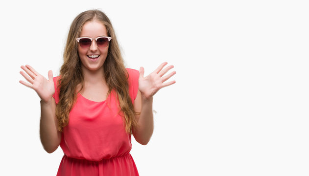 Young blonde woman wearing pink sunglasses very happy and excited, winner expression celebrating victory screaming with big smile and raised hands