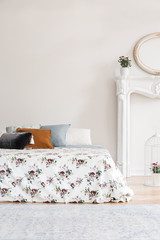 Feminine English style bedroom interior with a bed with rose pattern cover and multicolor pillows against an empty copy space wall. Real photo.